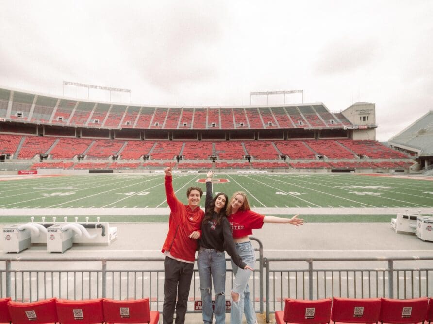 3 people excited in The Shoe, in front of the football field