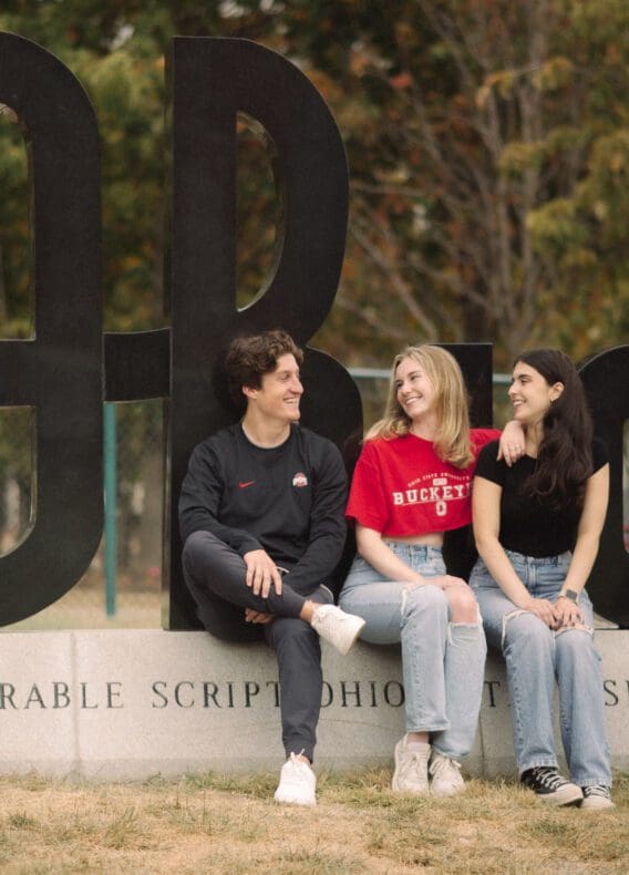 3 students sitting on script ohio on OSU campus