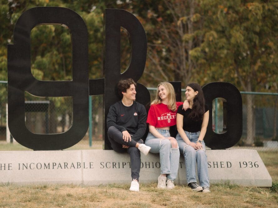 3 students sitting on script ohio on OSU campus